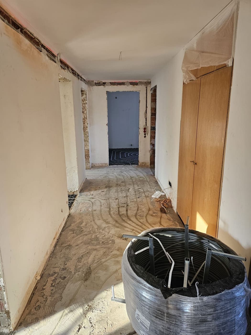 Derselbe Flur in einer späteren Phase: die Leerrohre sind eingebettet, im Hintergrund ein Raum mit verlegter Fußbodenheizung.